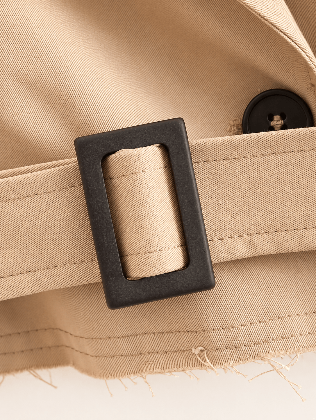 Gros plan sur la boucle rectangulaire brun foncé et le bouton, veste trench camel